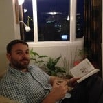 Luke relaxes with a beer and a book, the night lights of Manila shine in the distance